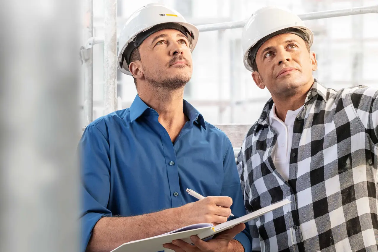 Close-up of a Sto advisor and a tradesman on a construction site. Both are wearing white helmets.